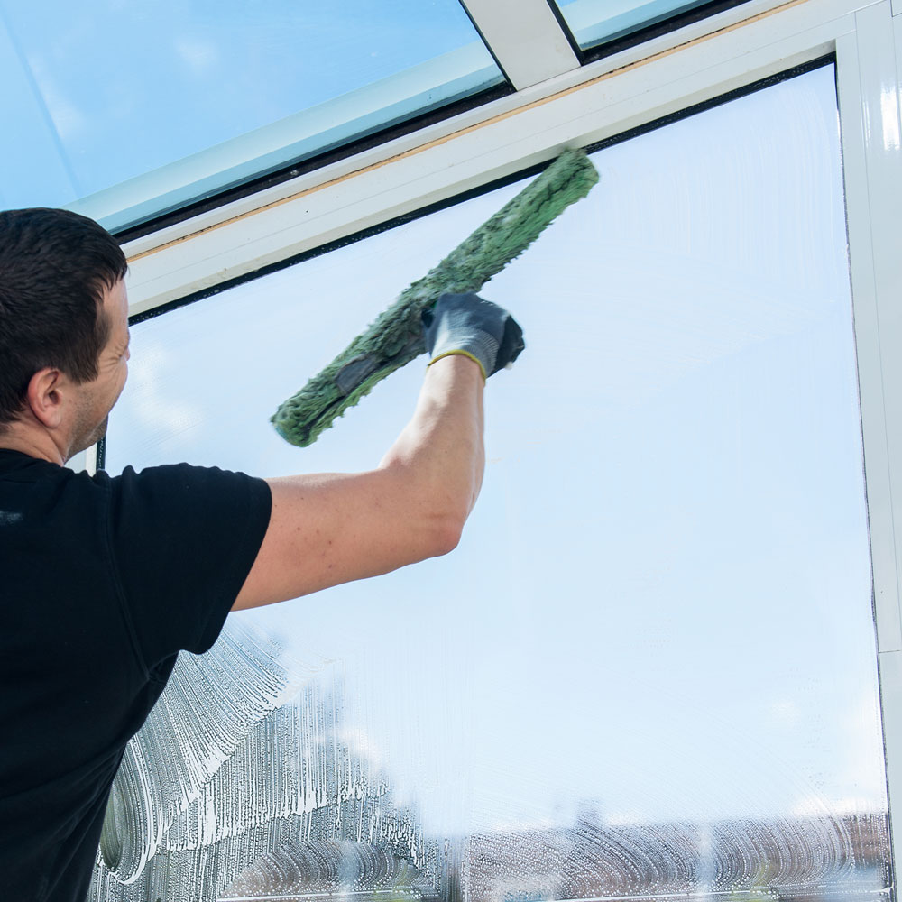 Ein Mann reinigt mit einem Fensterwischer eine Glasscheibe.