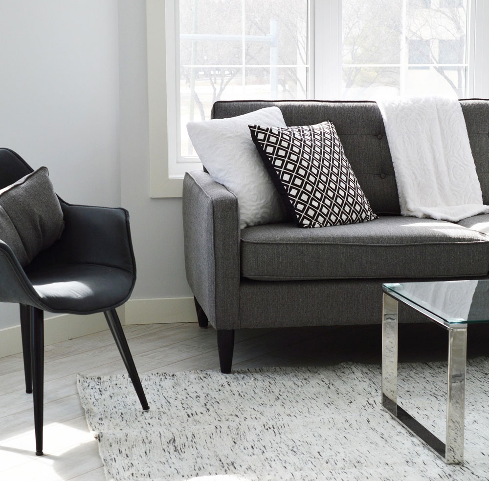 Ein modern eingerichtetes Wohnzimmer, im Anschnitt zu sehen ein Stuhl und ein Sofa vor einem Glastisch.